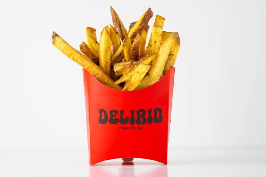 Patatas fritas doradas en un envase rojo con el logo de Delirio Smash Burger